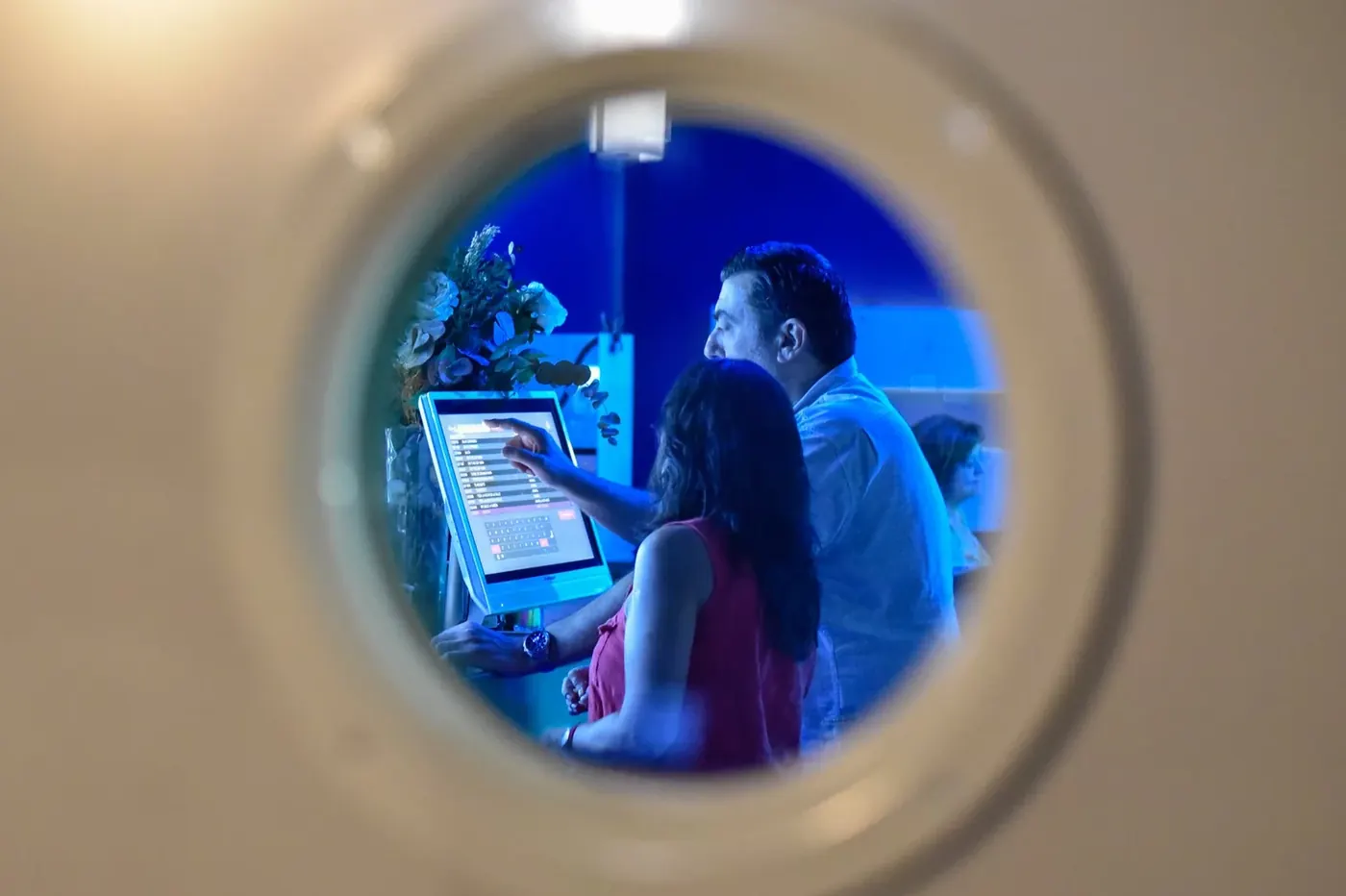 Una pareja eligiendo canción en la pantalla, vista a través de un ojo de buey